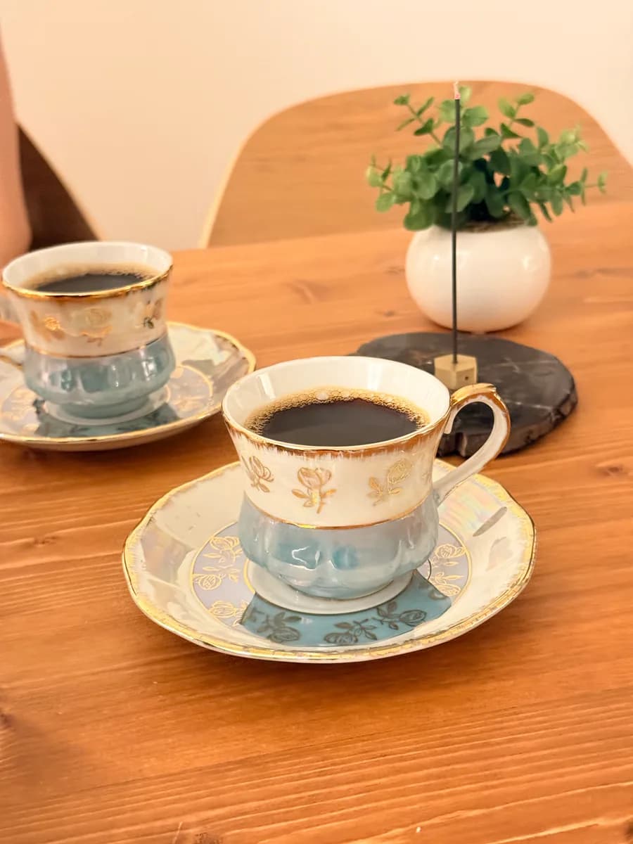 木のテーブルに並ぶ、みおが事務所で淹れてくれたコーヒー2杯。白と水色の金縁のカップとソーサー