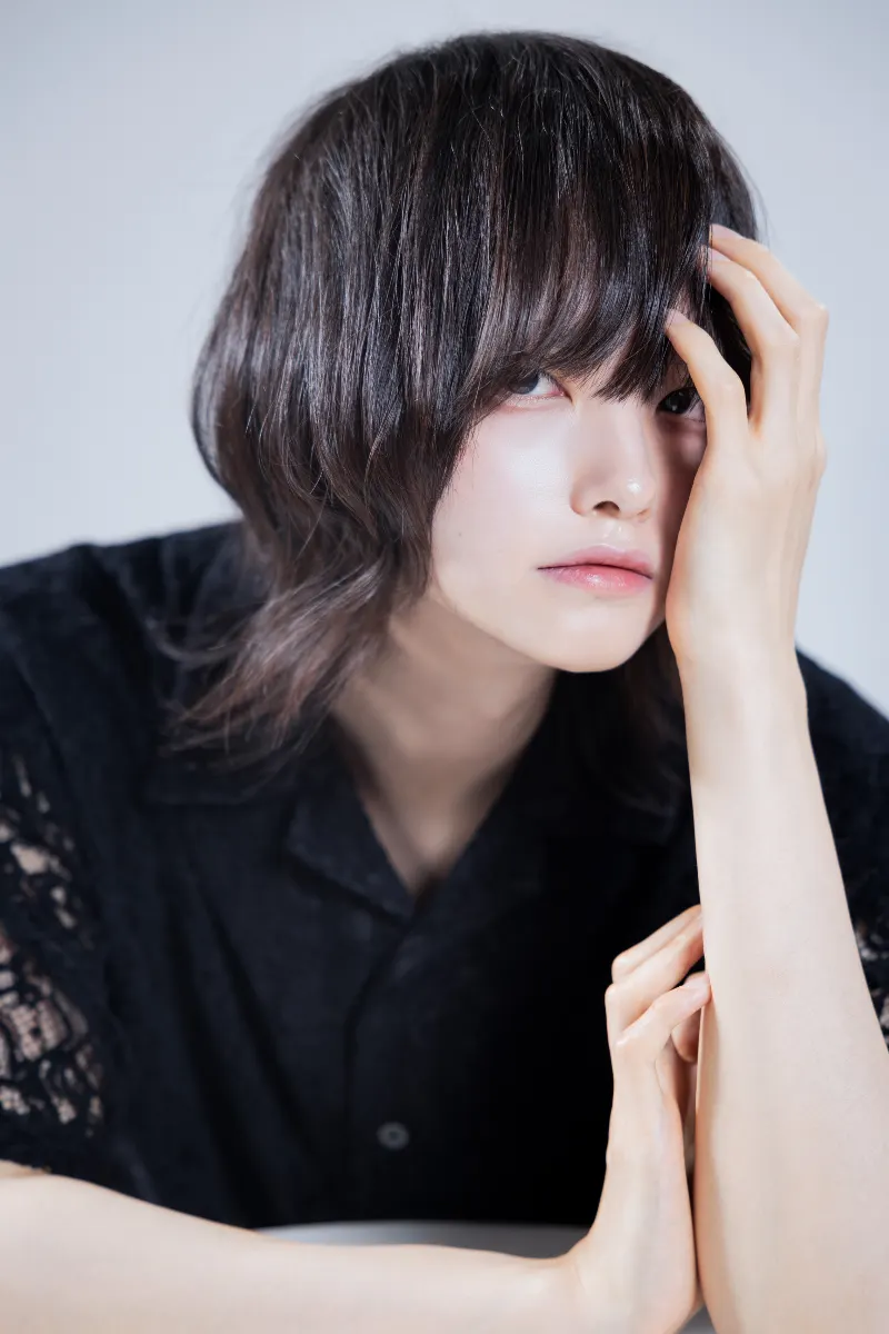 黒いシャツ姿で額に手を添え、横を見つめる男性